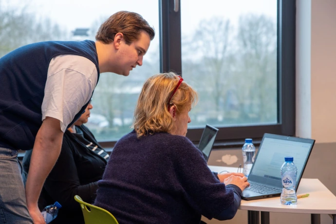 AI trainer geeft een deelnemer persoonlijke begeleiding achter de laptop tijdens een praktische cursus.